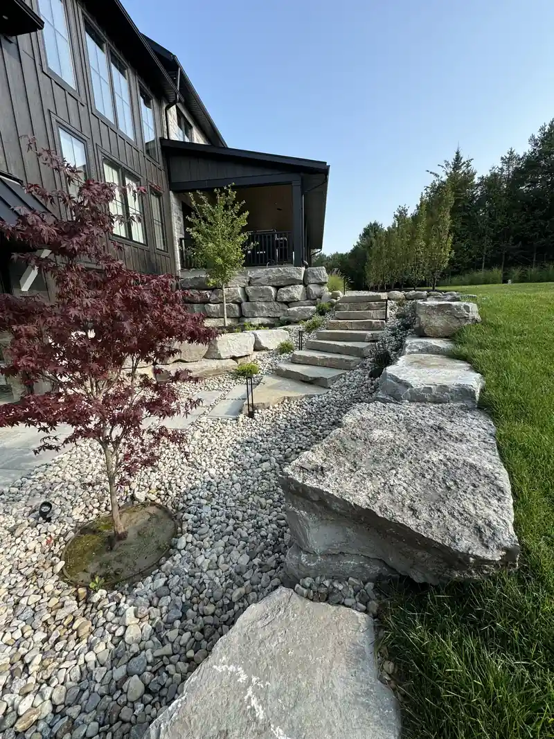Armour stone steps and boulders beside a river rock bed with a Japanese maple
